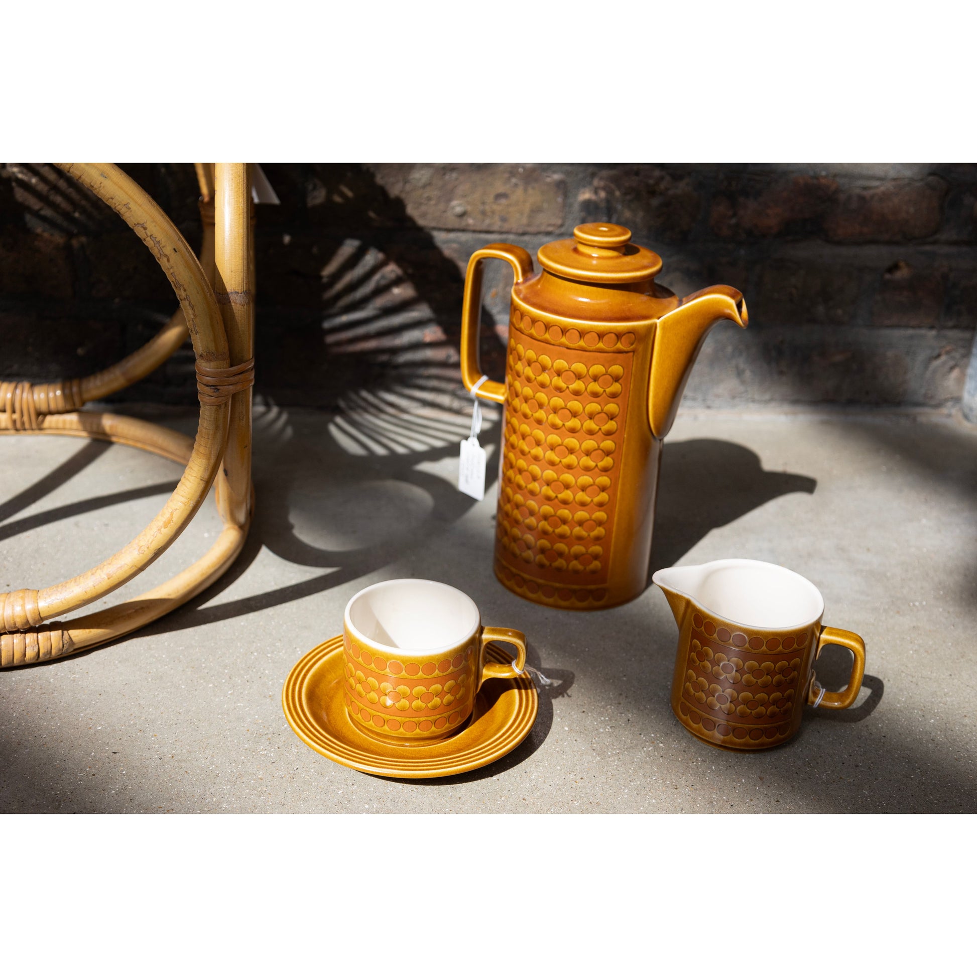 Brown ceramic coffee set with a carafe, cup, and saucer on a stone surface.