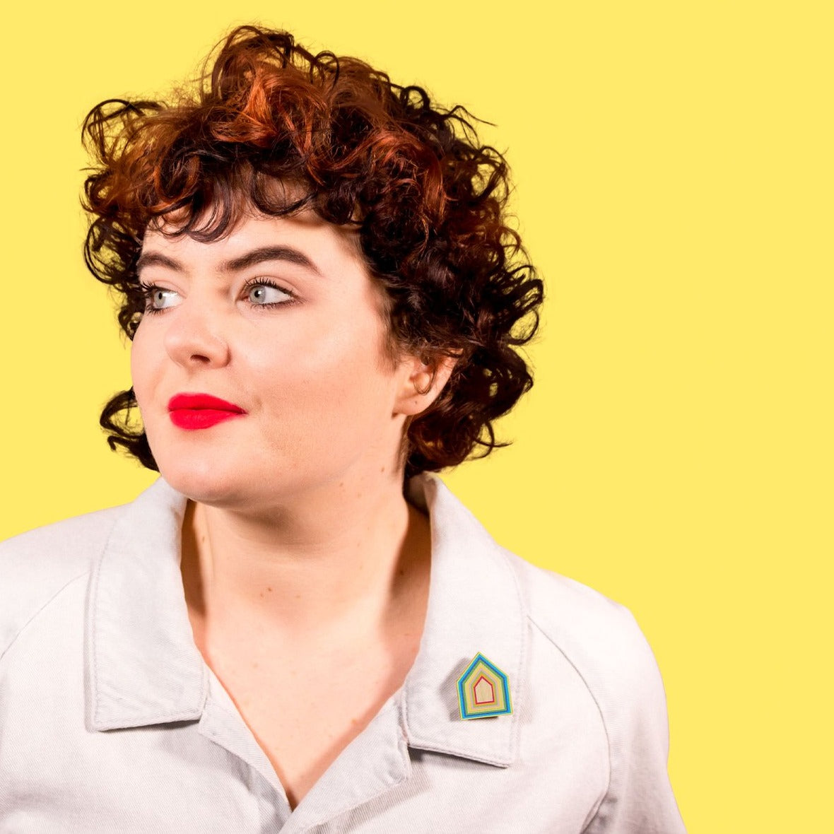 Figure is seen wearing wooden brooch on their collar against a yellow background.