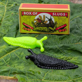 Green and black plastic slugs against a leaf; in the background is a match box labelled 'Box of Slugs'.