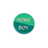Close up of Home Boy badge with half light green and half dark green background separated diagonally. With 'Home boy' in light peach font. 