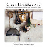 A white book, on the cover there is photograph of different craft utensils and herbs hanging from a wooden stick. In black font on top it reads "Green Housekeeping" and below in smaller font "Recipes and solutions for a cleaner, more sustainable home."