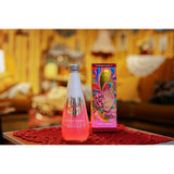 A pink bottle of bath soak with its box behind. They are both sitting on a red tapestry and in the background there is a yellow living room from the 70s.