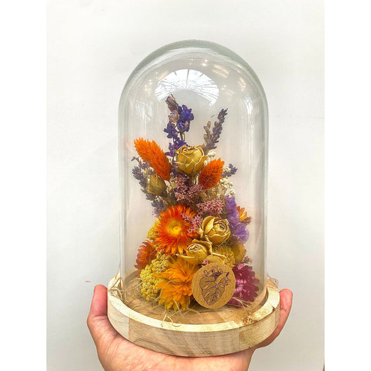A hand holding a jar with dried flowers in colours orange, purple, yellow and green.