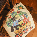 A bag with a folk illustration of cats dancing. The bag rests on a wooden chair.