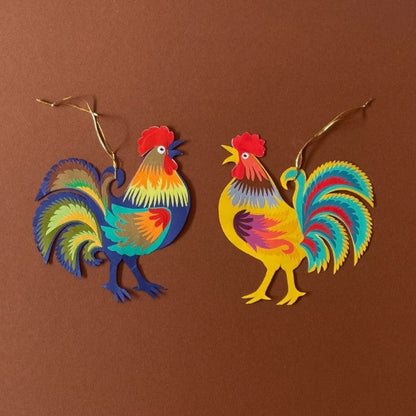 Two colourful paper cockerels decorations on a brown background.