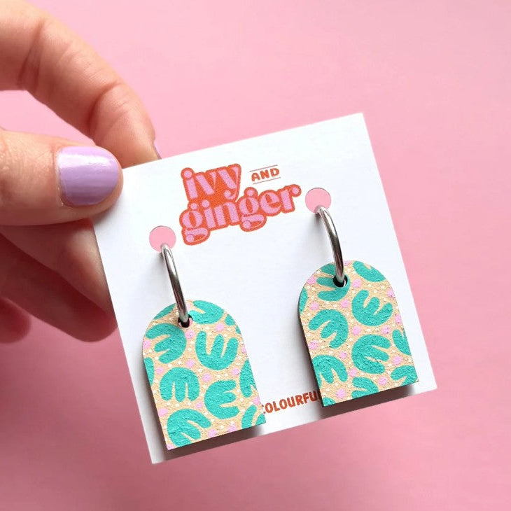 Pair of earrings on a 'Ivy and Ginger' branded card against a pink background