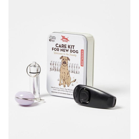 A care kit for a new dog inside a small metal box on a white background.  Next to it, there is an identification charm, a dog whistle and a clicker collar light. 