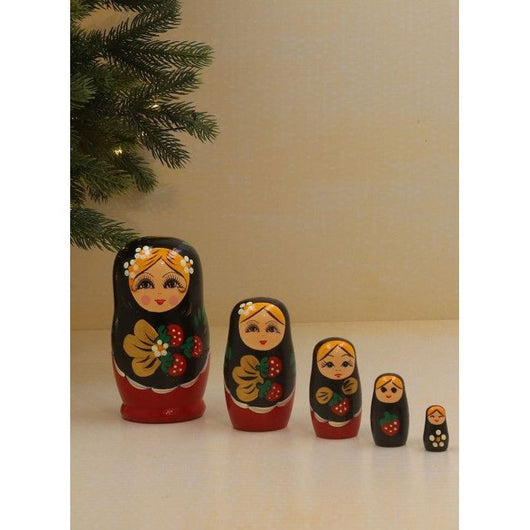 Five matryoshka dolls painted by hand, lined up by size from big to small under a Christmas tree branch.
