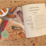 An open book on a wooden table. On the left page there is a picture of home made dog treats and on the right page the instructions on how to make "Vegan Dog Treats" can be read.