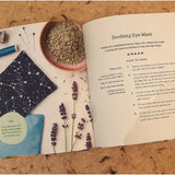An open book on a wooden table. On the left page there is a picture of craft utensils, lavender and seeds sit on a white background. On the right page the instructions of how to make a "Soothing Eye Mask" can be read.
