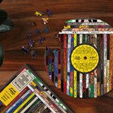 A puzzle being completed, revealing the shape of a circular record. The box of the puzzle sits beside the part-completed puzzle on a wooden table, revealing the design feautring hiphop record names