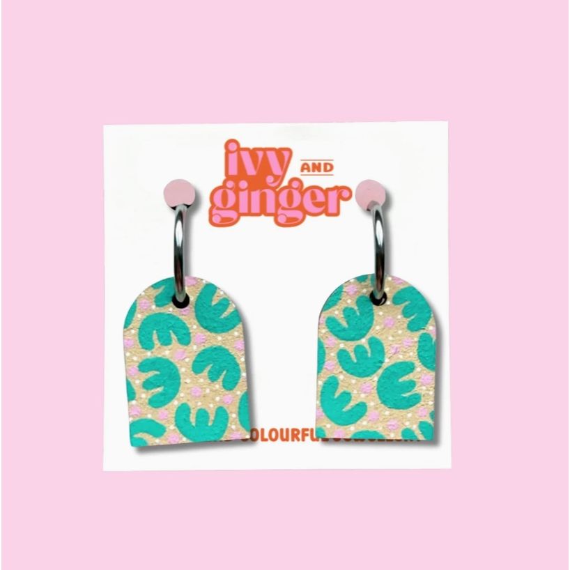 Pair of earrings with green leaf pattern on a 'ivy and ginger' branded card against a pink background