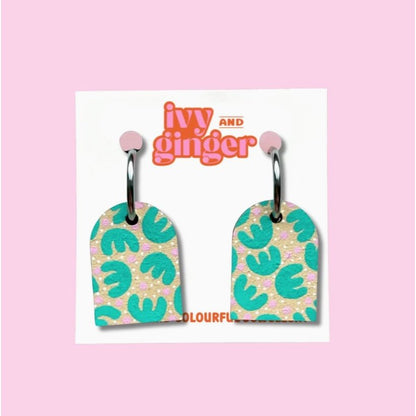 Pair of earrings with green leaf pattern on a 'ivy and ginger' branded card against a pink background