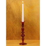 A red candle holder with oval details and a white candle on it. The background is golden yellow.