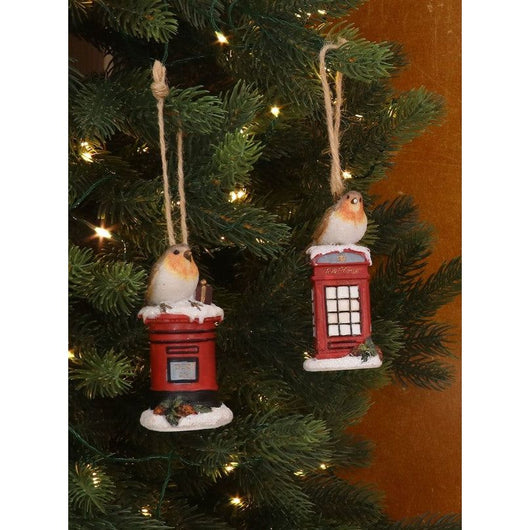Two ornament decorations of a robin bird hanging on a Christmas tree with fairy lights. One of the robins is on a post box and one is on a telephone cabin. 