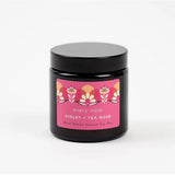 A Violet and Tea Rose Candle on a white background. The container is black glass with a plastic black lid. The label is pink with illustrations of roses in shades of pink, orange and cream details.  In small black font it reads "Hand poured natural soy wax."