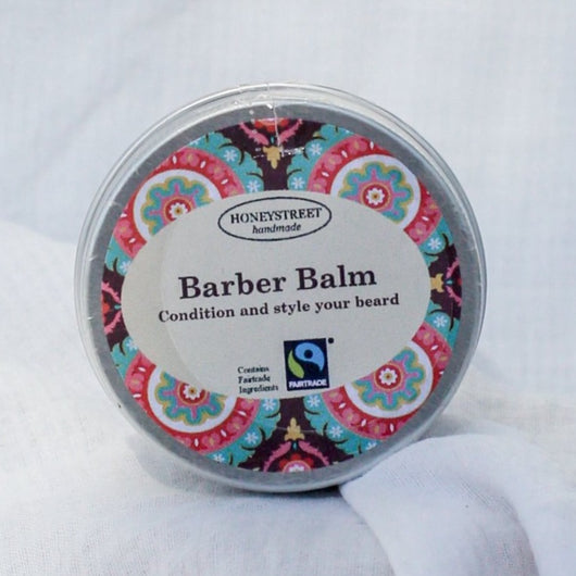 Round tin of Barber Balm in silver with geometric pattern. The label reads ‘condition and style your beard’ and displays a Fairtrade label. 