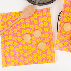 reusable greaseproof paper against a white background; the paper is red with yellow flowers and a wooden spoon is seen on top of it.