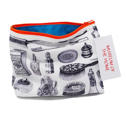 White cosmetics bag printed with illustrations of perfume bottles and hairbrushes in an illustrative style. The bag has an orange zip and a blue lining. 