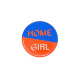 Close up of Home Girl badge with half blue and half red background, separated diagonally. With 'Home' in red and 'Girl' in off white font.