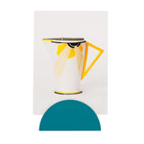 Dark green half circular photo clip holding museum of the home 'Vogue teapot in sunray' postcard. Postcard is of white teapot with abstract sunray, black rims and yellow handle. 