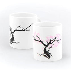 On a white background, two white mugs with a blossom tree with pink leaves.