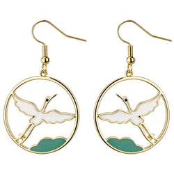 A pair of rounded golden earrings with a white flying crane inside and a green detail under it.