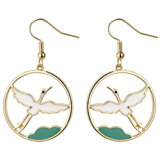 A pair of rounded golden earrings with a white flying crane inside and a green detail under it.